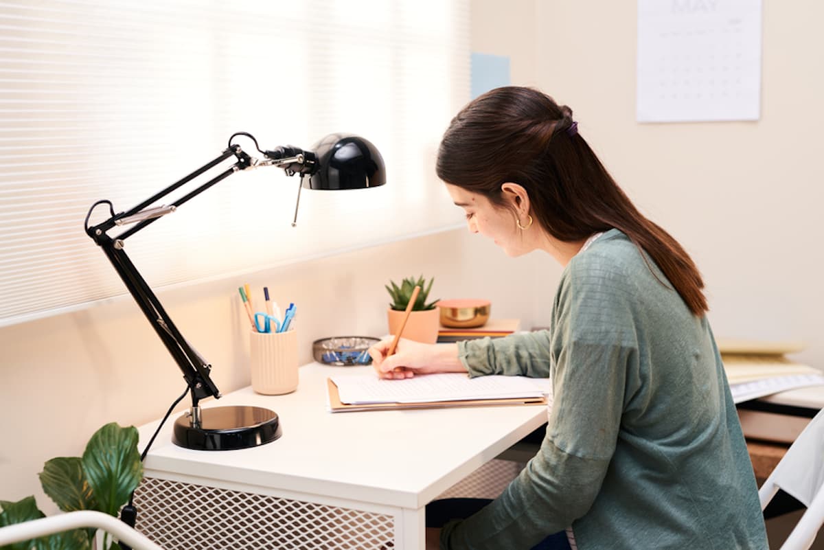 A brunette woman seated at a desk smiles as she fills out paperwork.