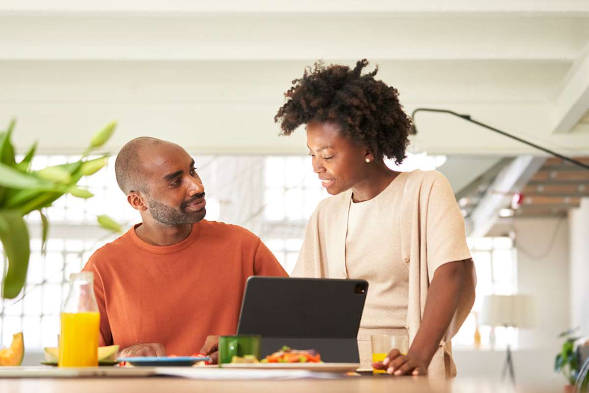 Smiling wife and husband have a conversation at breakfast table with tablet on